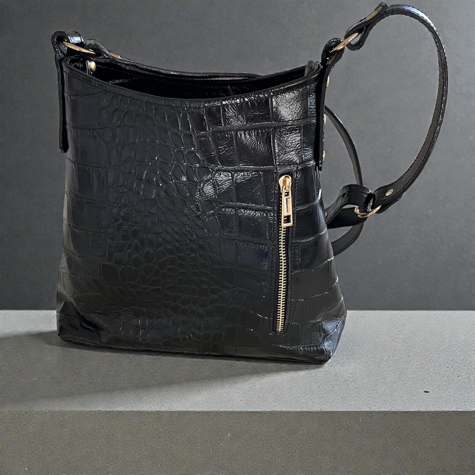 Black leather handbag on a gray surface with a gold zipper detail.