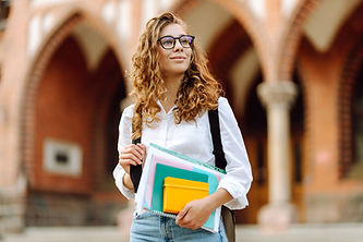A young woman student with curly hair holds several colorful notebooks while standing outs