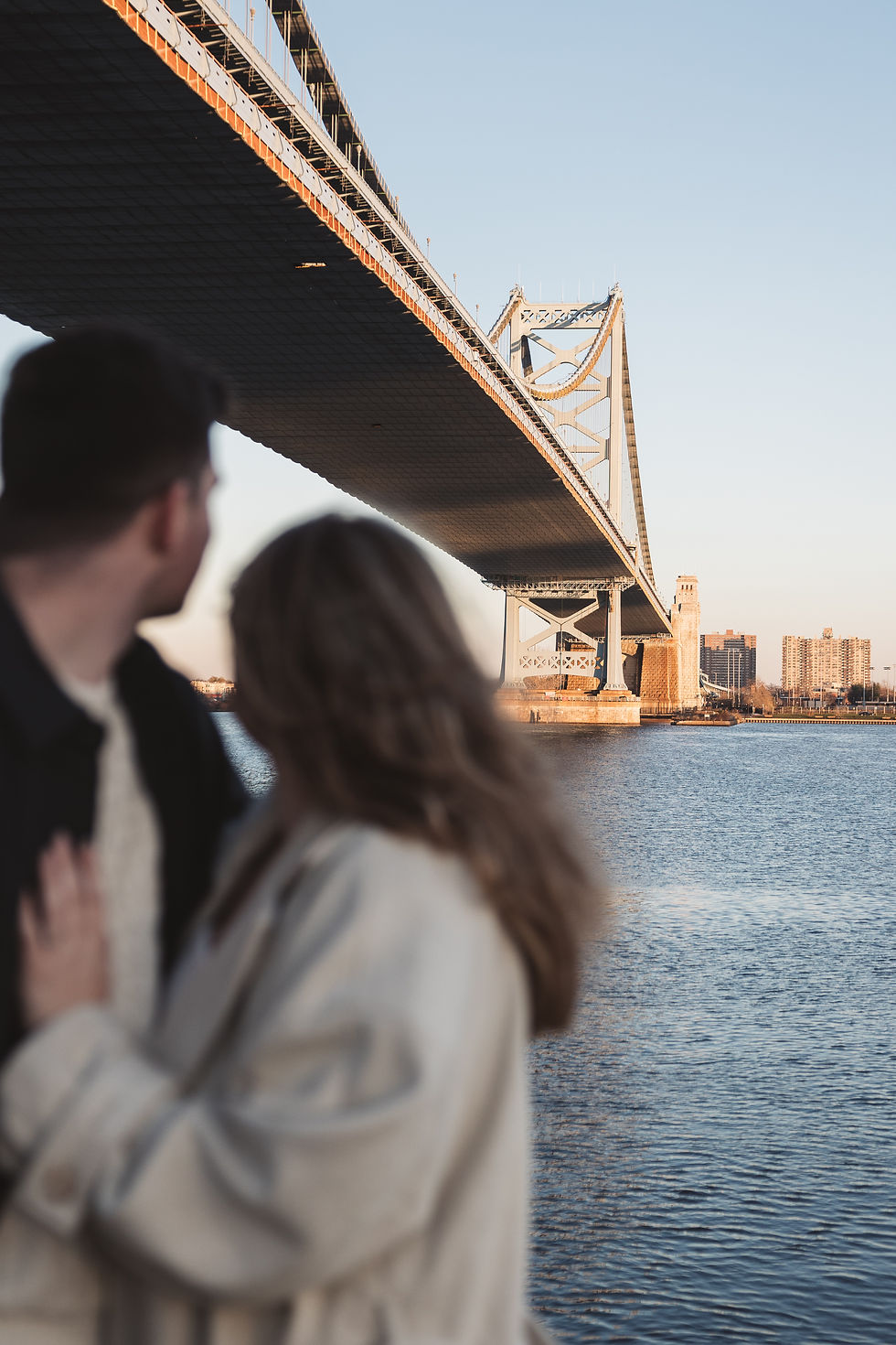 A couple stand together and look out at the Ben Franklin Bridge from Race Street Pier. Taken by Philly wedding photographer Madison Neumann Photography.