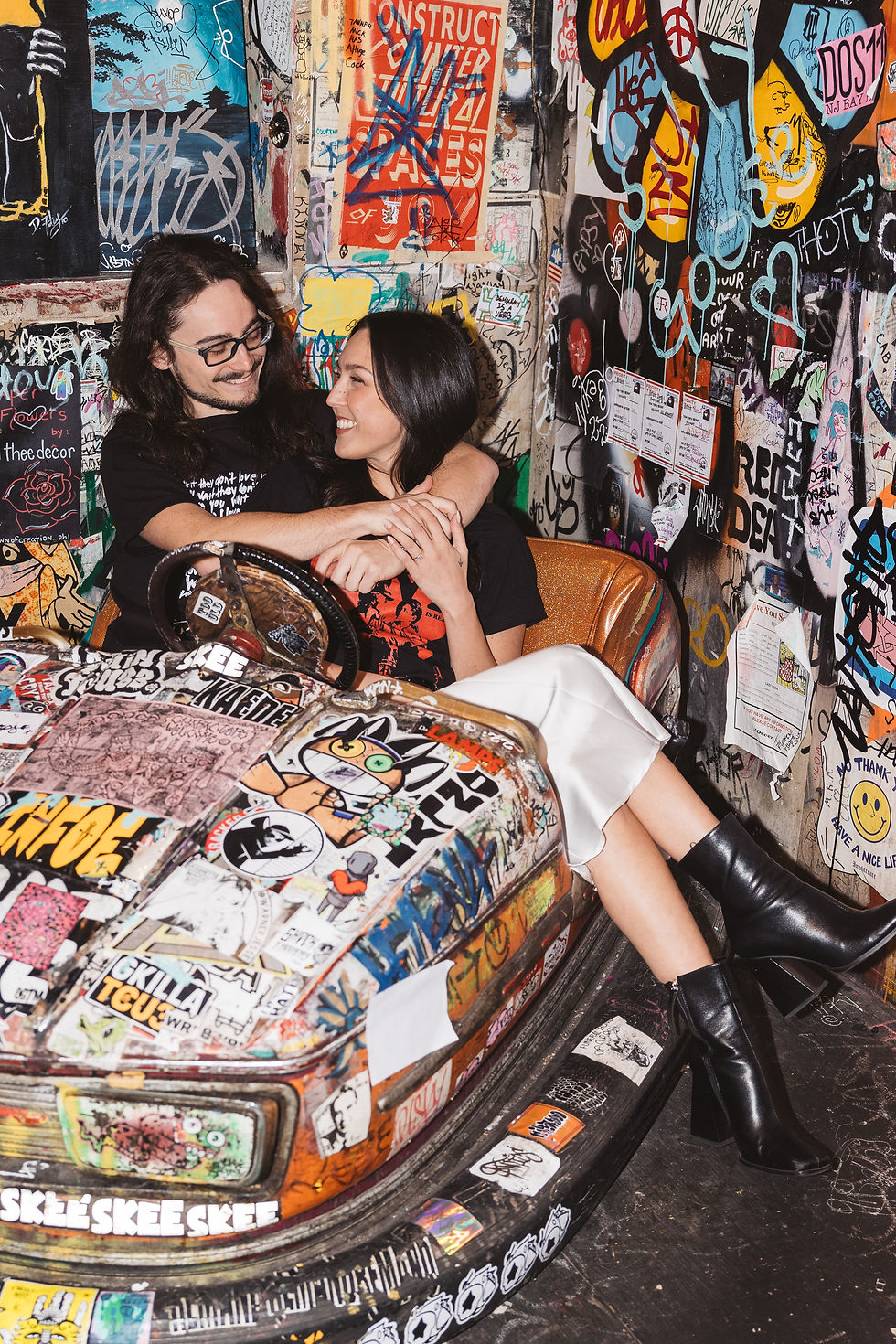 Future bride and groom sit in decorative bumper car in Tattooed Mom bar in Philadelphia, PA. Engagement session portraits photographed by South Jersey, Philly based wedding photographer Madison Neumann Photography.