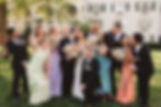 Wedding party celebrates as bride and groom embrace on their wedding day. Bridesmaids wear pastel colored gown, groomsmen wear black tuxedos. Colorful wedding bouquets in front of white building of venue. Photographed by South Jersey, Philadelphia based wedding photographer Madison Neumann Photography.