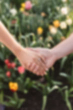 Newly engaged couple holding hands with tulip field in the background. Future bride wears ring holding the hand of her future groom after proposal. Photographed by South Jersey, Philadelphia based wedding photographer Madison Neumann Photography.