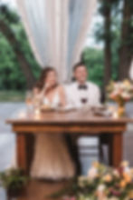 Bride and groom smile during speeches at sweetheart table for wedding at Bartram's Garden in Philadelphia, PA. Photographed by South Jersey Philly wedding photographer Madison Neumann Photography.