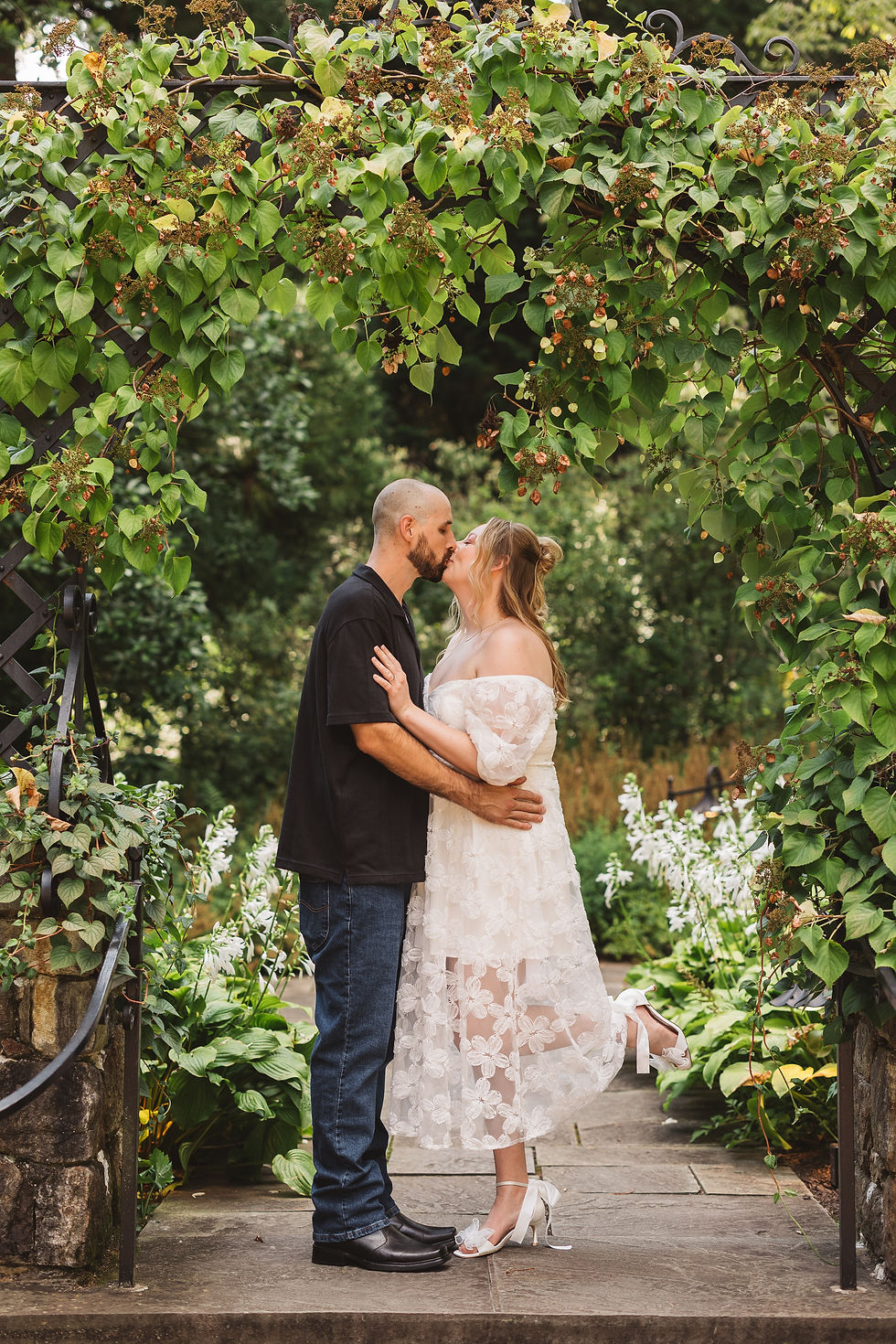 Fiancées pose together under greenery and vines in a garden. Engagement session at Winterthur Museum, Garden and Library in Winterthur, Delaware. Photographed by South Jersey, Philadelphia based wedding photographer Madison Neumann Photography.