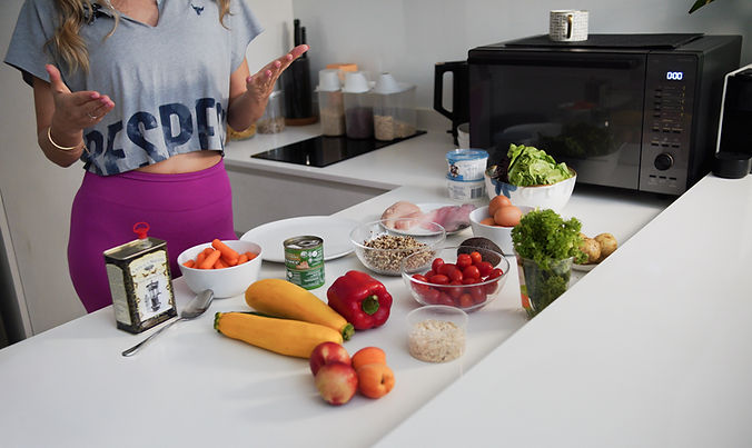 Woman gesturing in kitchen with various fresh ingredients.