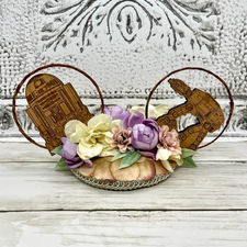 A mouse ear headpiece that converts from headband to clip-in, but looks like a vintage round fascinator with round wire mouse ears. The headpiece is decorated with pastel flowers, sage and gold trim and wooden Star Wars ornaments.