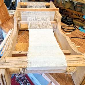 A tabletop hand loom weaving a length of linen cloth