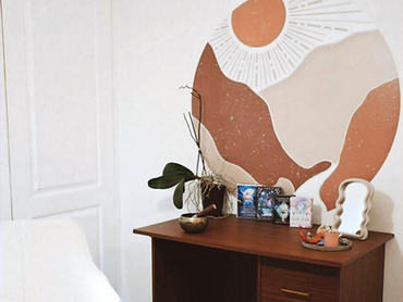 Bureau en bois dans le cabinet chaleureux de Pauline, avec bougie, bol tibétain et cartes oracles, fresque soleil terracotta.