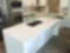 A marble island with a completely white finish in the middle of an unfinished kitchen