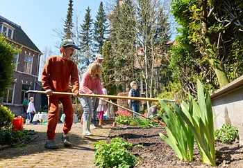 Leerlingen harken een moestuin op school aan.