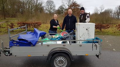 3 mensen staan achteraanhangwagen gevuld met zwerfafval
