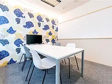 札幌ビレッジのミーティングルーム。カラフルなデザイン壁とホワイトボードがあり、6人用の白い会議テーブルとモニターを備えた打ち合わせスペース。