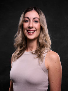 Studio portrait of blonde woman wearing sleeveless top smiling on dark background
