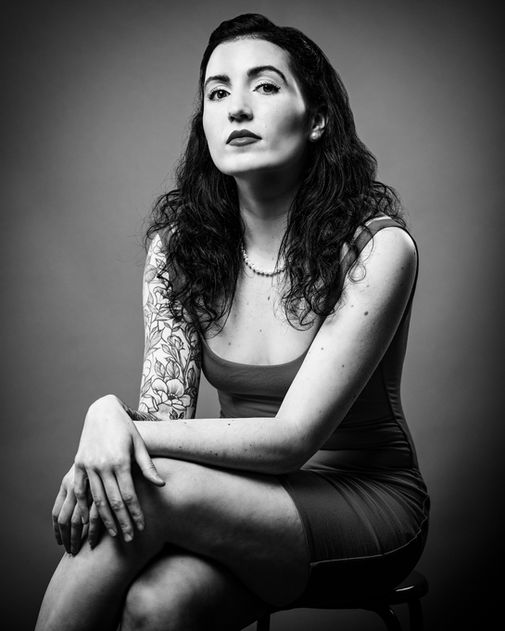 Black and white studio portrait of a woman sitting in a confident pose, looking at the camera.
