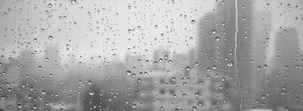 Rainy city view through a window, soft reflections and grayscale.