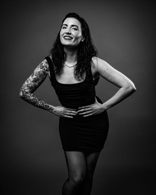 Black and white portrait of a woman in a black dress, hands on hips, looking self-assured.