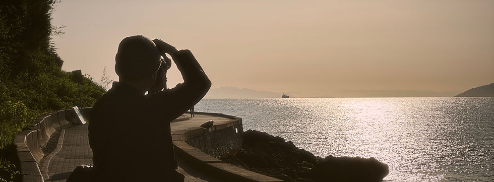 Photographer standing by the seawall during sunset, panoramic city and water view.