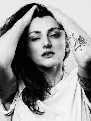Black and white portrait of Emily with hands in hair, soft expression and tattoo visible