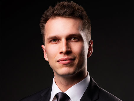 Close-up professional headshot of a man in a dark suit, looking confident against a dark blue background with dramatic lighting.