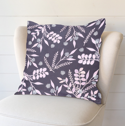 On a cream chair is an eye catching grey cushion that has a pale pink botanical leaf design printed on it.