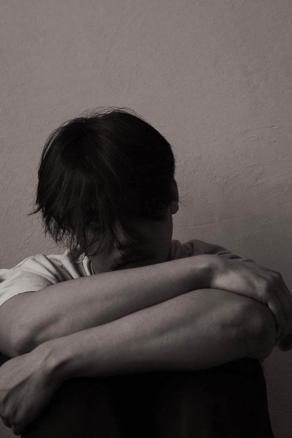 A person sitting with their head down, arms wrapped around their knees, conveying a sense of introspection and solitude in a monochrome setting.