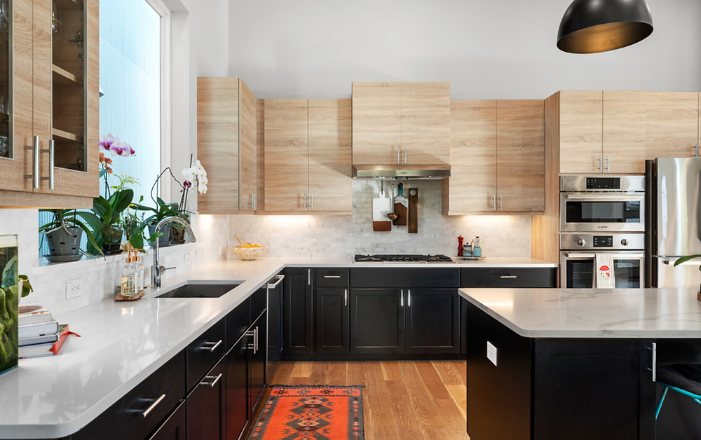 image of modern organic kitchen. light wood upper cabinets, black lower cabinets. white solid stone countertops
