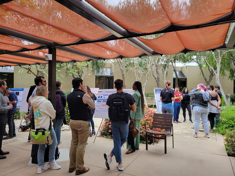 A person standing by their research posters, with a moderate audience.
