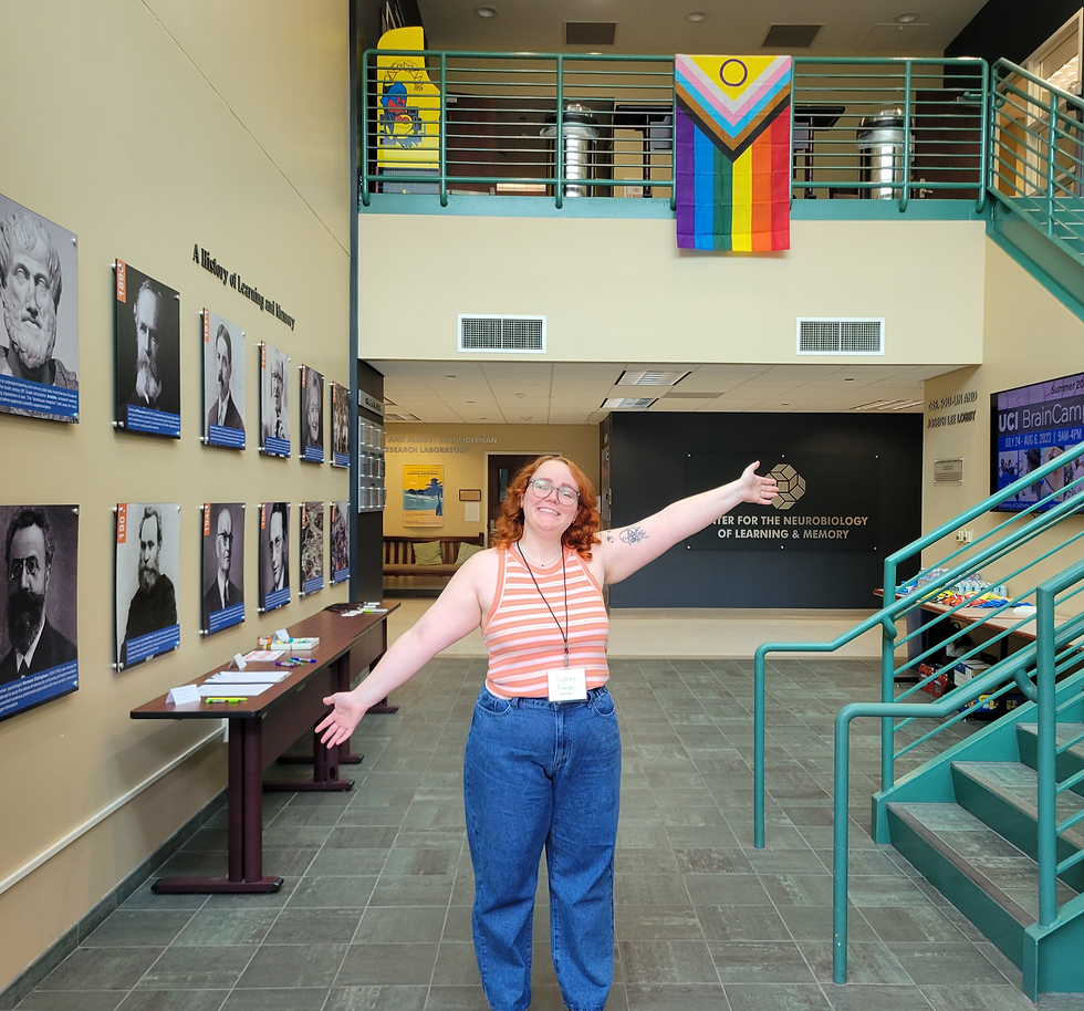 A person with their arms open, showing the greeting area of the QTABS symposium. A pride flag is hanging up the stairs directly above the person.
