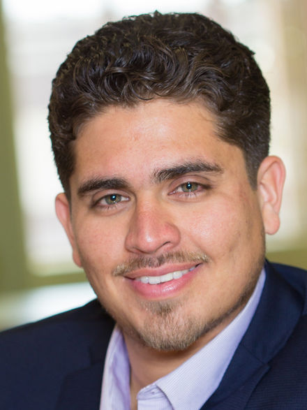 Man in a navy suit smiling, professional headshot