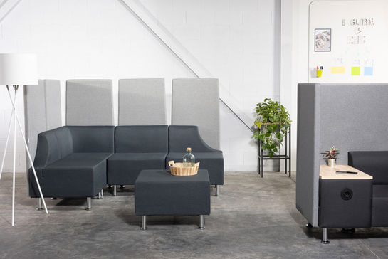 Dunkelgraues Modulsofa und Hocker im Büroraum.