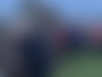 Michael and Steve stand smiling in front of a large stone in a field. A group in the background standing and holding hands in a circle.