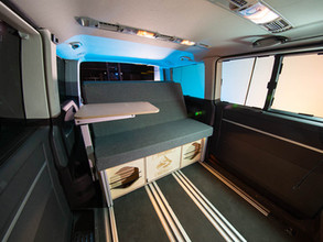 Innenraum eines VW T5 Bus mit dem Camperausbau RoadBoxx mit der Sitzbank und dem kleinen flexiblen Tisch.