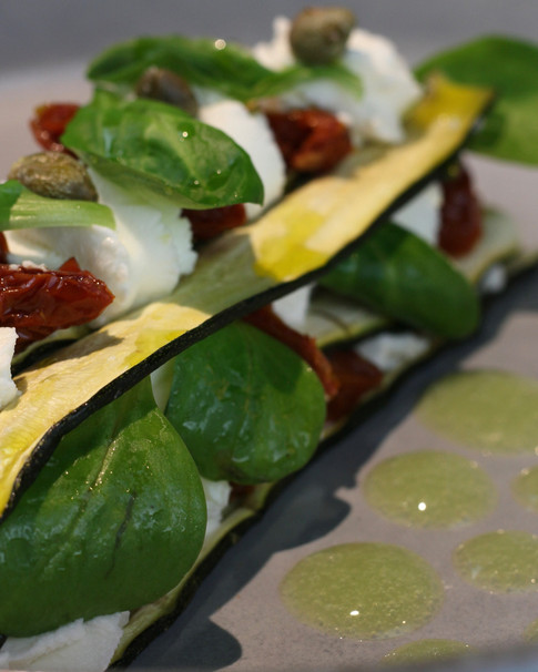 Parmigiana estiva di zucchine in soia, caprino, pomodori secchi, capperi e mais tostato