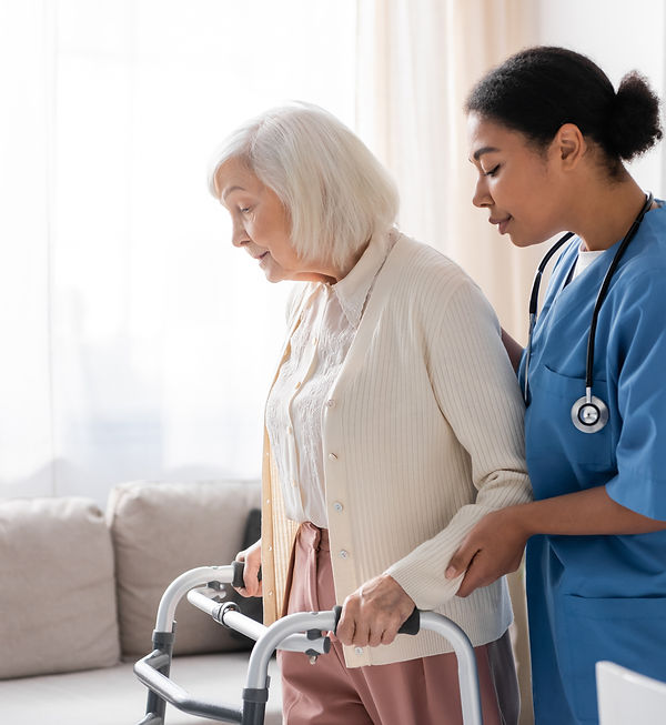 brunette multiracial nurse in uniform supporting retired woman with grey hair walking with