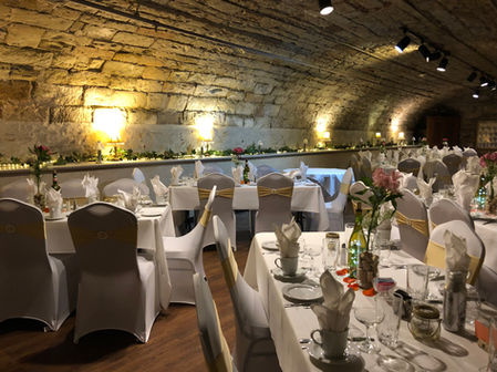 Elegant banquet room with arched stone ceiling, white tables, gold sashes.