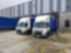 Two DAF trucks parked at a warehouse loading bay
