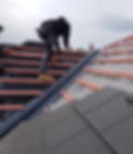 Roofer in black workwear fixing tiles on a pitched roof