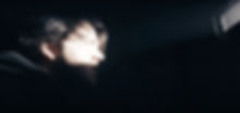 A side profile of a person's face lit by a beam of light in a dark room