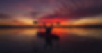 Kayaker raises paddle triumphantly against a vibrant red and purple sunset over calm water, creating a serene and triumphant mood.