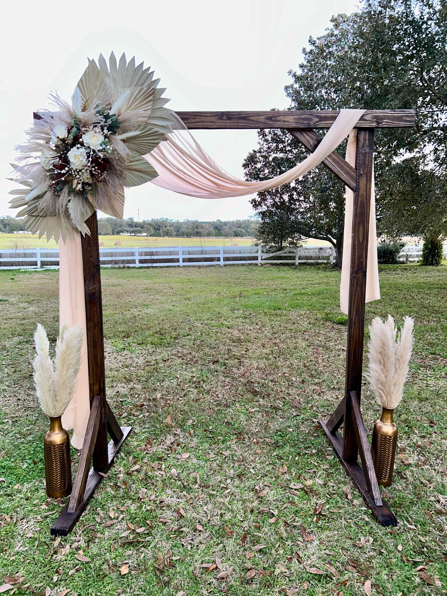 Wooden wedding arch decorated with flowers and fabric, set outdoors on grass.