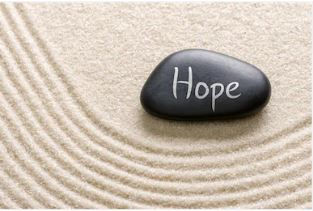 A black stone with "Hope" written on it rests on raked sand in a zen garden, creating a calm, serene atmosphere.