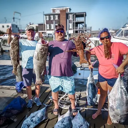 Two customers and Cindy from Instigator standing on a pier in Swansboro holding their catch, multiple fish species and lobsters, in North Carolina
