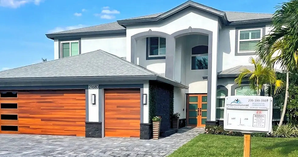 Modern house with grey roof and wood garage doors. A Difilippo construction sign with contact details is in the front yard. Palm tree nearby.