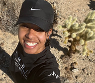 Kendra Esparza-Harris is a black woman with freckles. She has a nostril piercing and multiple ear piercings with silver jewelery. She is wearing a black t-shirt and a black Nike cap that covers her hair.