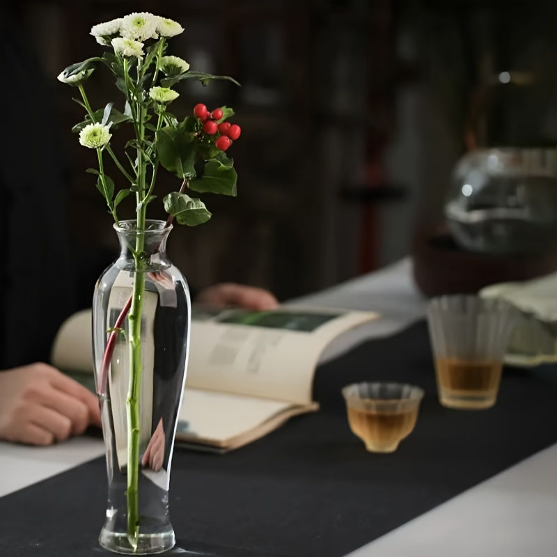 Thumbnail: Vase of white flowers and red berries on a table next to a person reading.