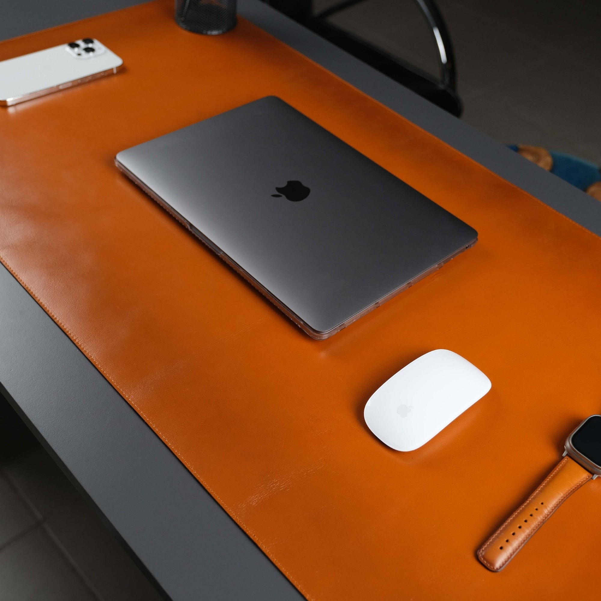 Closed laptop, mouse, phone, smartwatch on orange mat