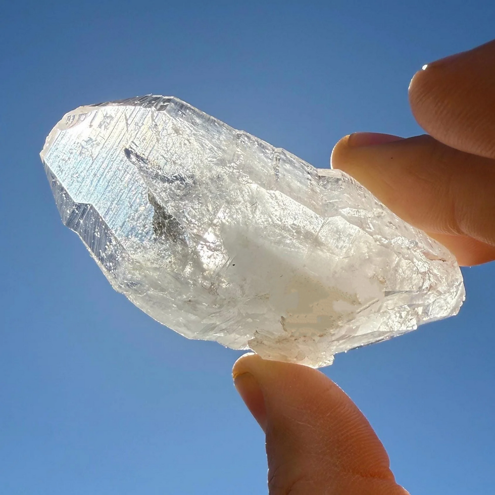 Hand holding clear crystal against blue sky