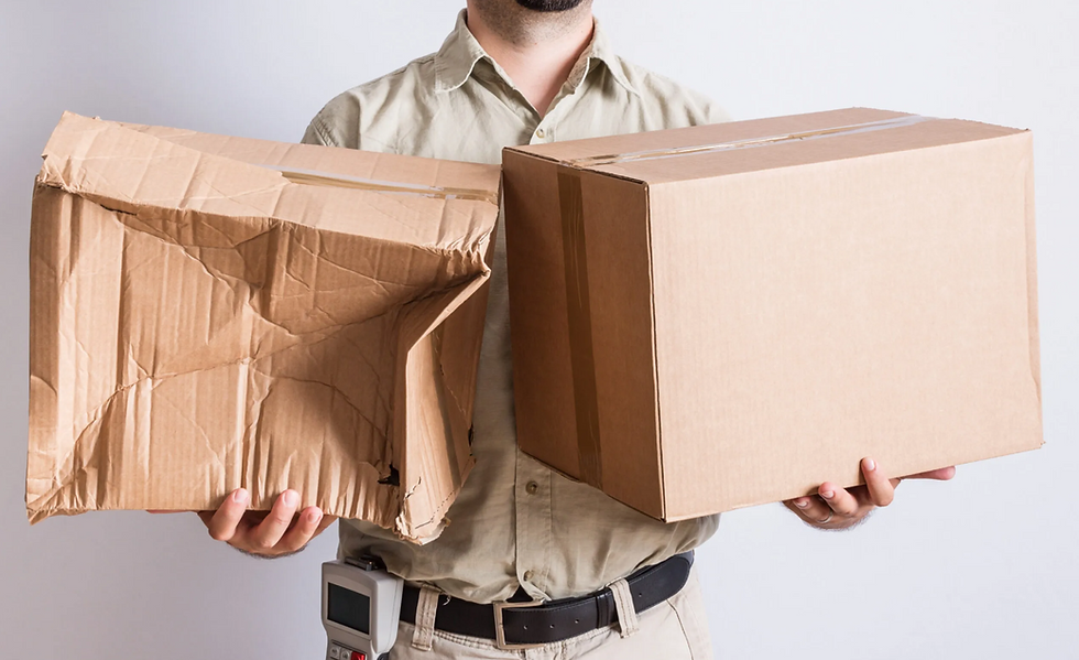 Man holding a crushed box in one hand and a sturdy box in the other, against a plain background. He wears a beige shirt and pants.