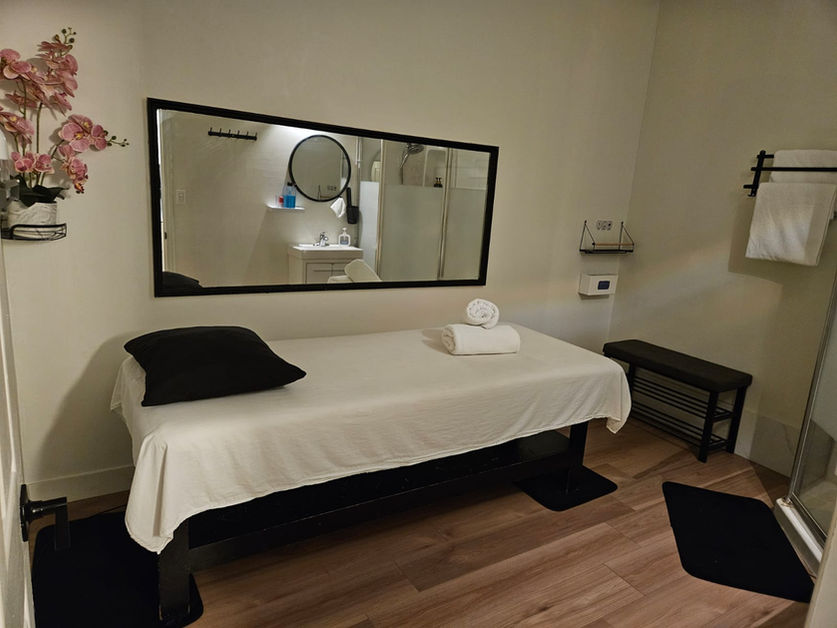 Elegant and serene massage room at Lily Skin & Body Care in North Vancouver, featuring a neatly prepared massage table, a full-length mirror, soft lighting, and delicate floral accents to create a calming and inviting environment.