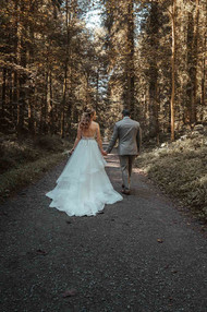 Hochzeit Erika und Demetris - Das Brautpaar läuft Hand in Hand auf einem Waldweg davon.